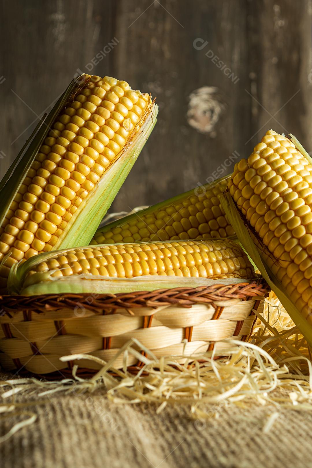 delicioso milho amarelo cru com folha verde e espiga, sobre canudos secos e superfície de madeira. tiro vertical