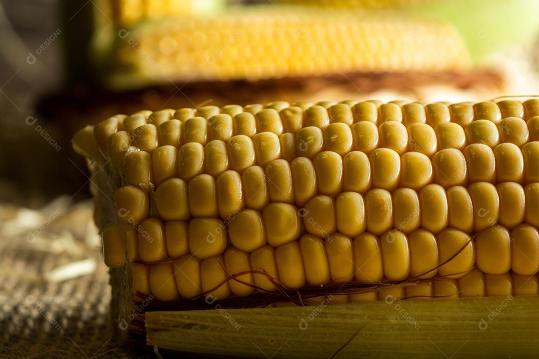 delicioso milho amarelo cru com folha verde e espiga, sobre canudos secos e superfície de madeira