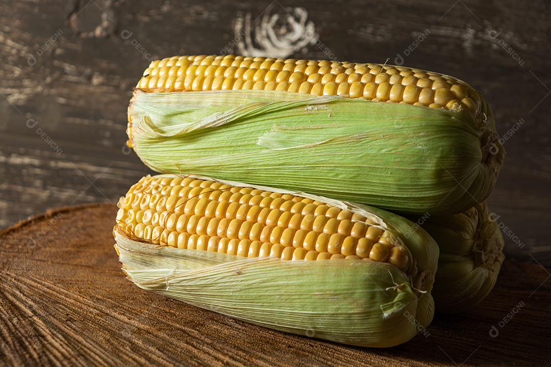 delicioso milho amarelo cru com folha verde e espiga, sobre canudos secos e superfície de madeira