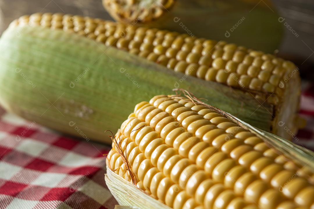 delicioso milho amarelo cru com folha verde e espiga, sobre canudos secos e superfície de madeira