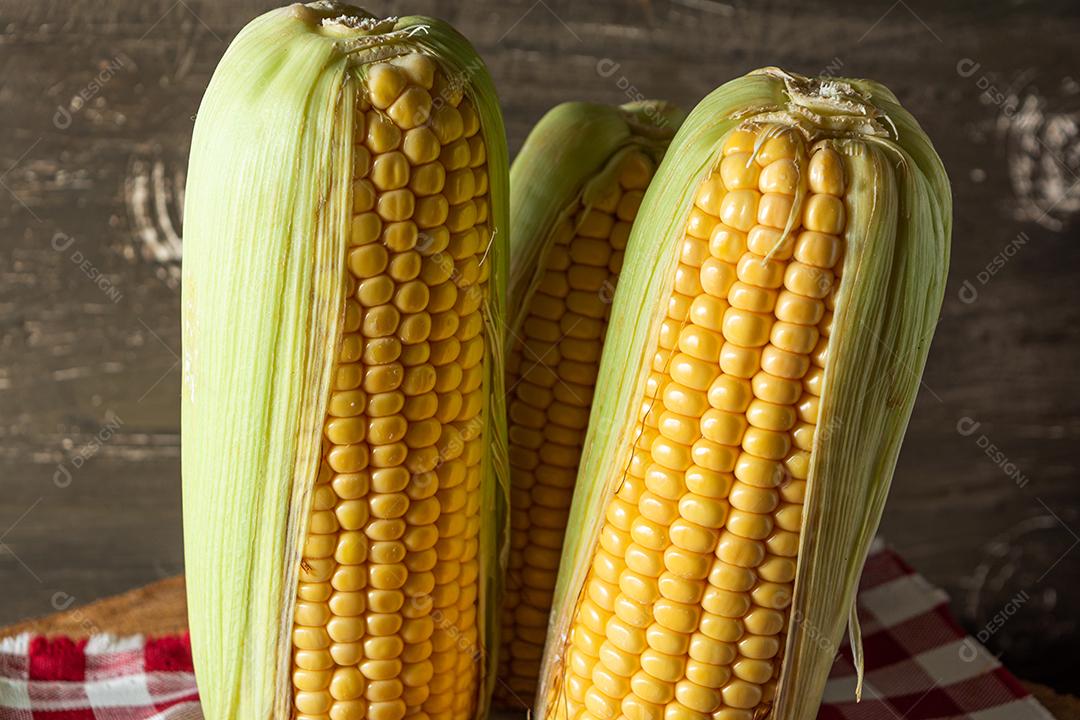 delicioso milho amarelo cru com folha verde e espiga, sobre canudos secos e superfície de madeira