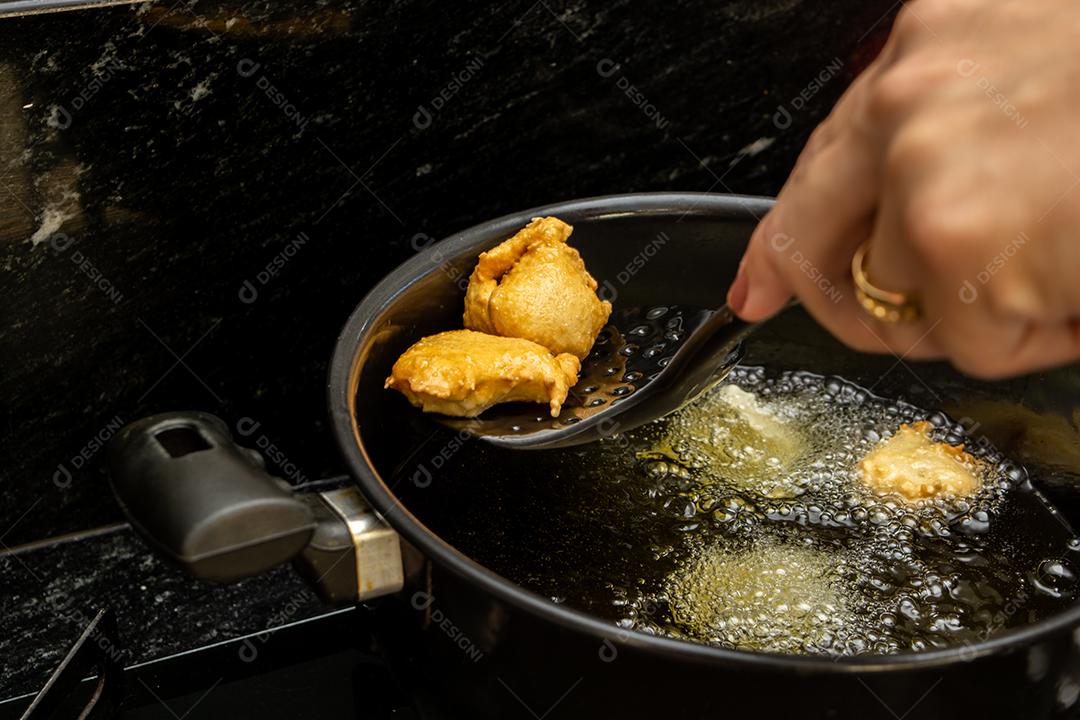 pegando a massa frita conhecida como bolinho de chuva com uma escumadeira. lanche típico e tradicional brasileiro.