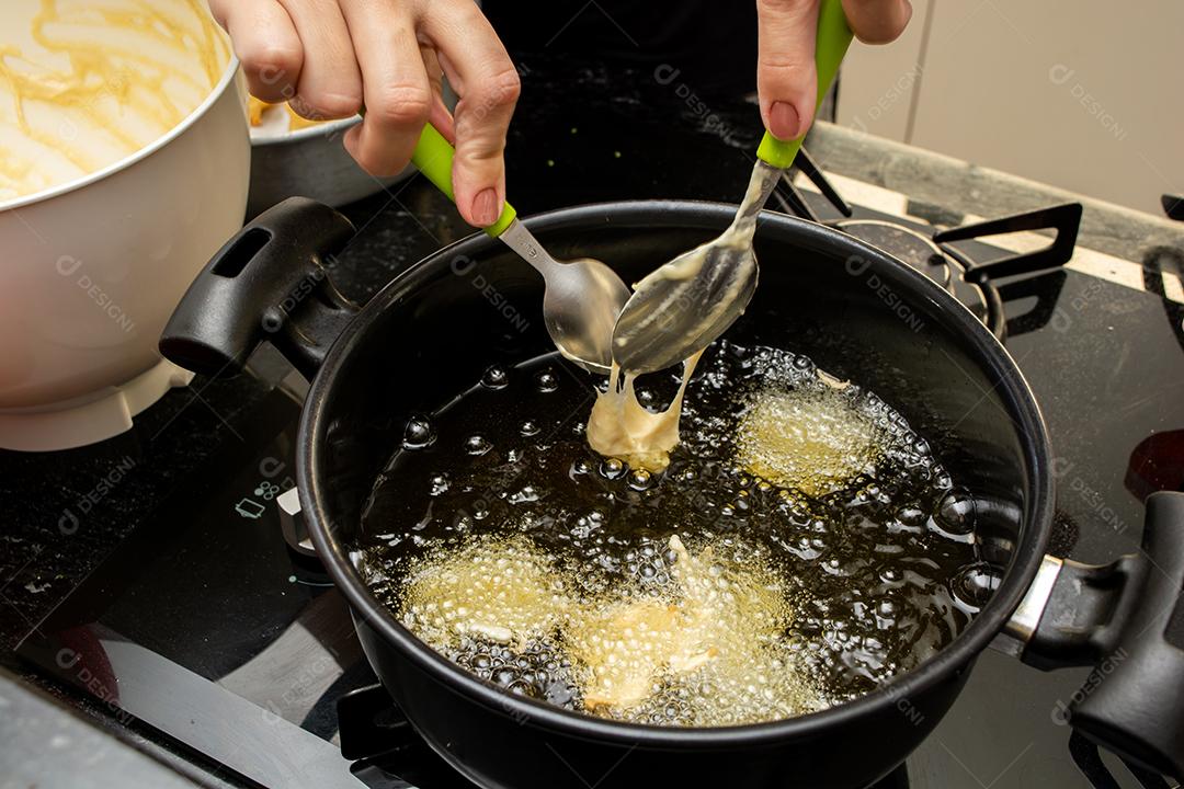 usando duas colheres para fritar a massa no óleo, para uma receita típica brasileira chamada bolinho de chuva