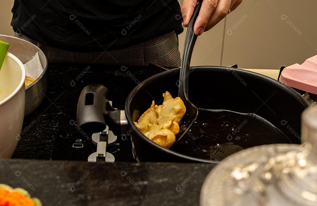 pegando a massa frita conhecida como bolinho de chuva com uma escumadeira. lanche típico e tradicional brasileiro.