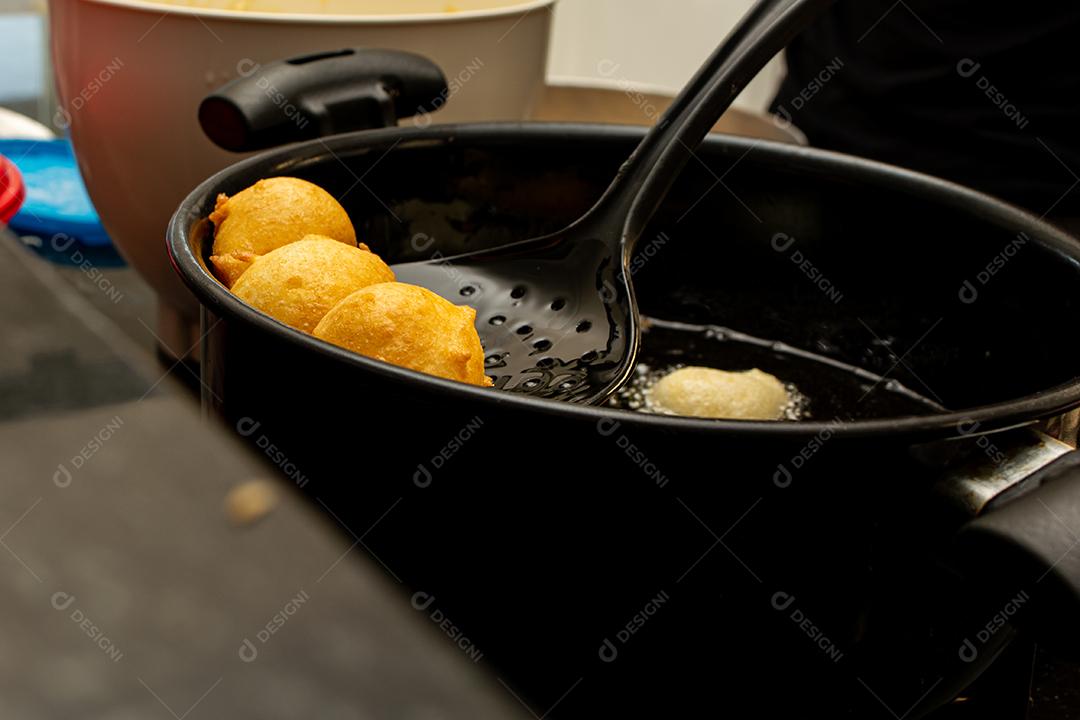 pegando a massa frita conhecida como bolinho de chuva com uma escumadeira. lanche típico e tradicional brasileiro.