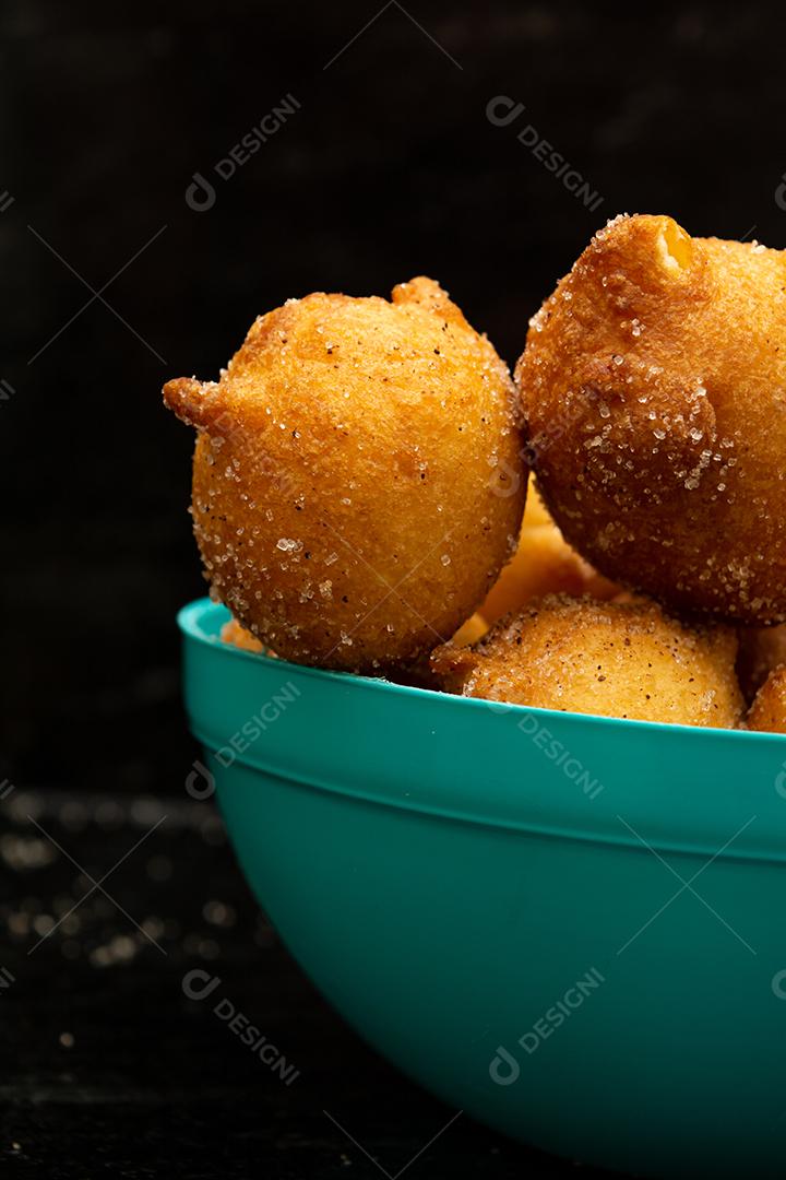 bolinho de chuva, receita tradicional brasileira, feita de massa frita com açúcar e canela, em pote azul e fundo preto. tiro vertical