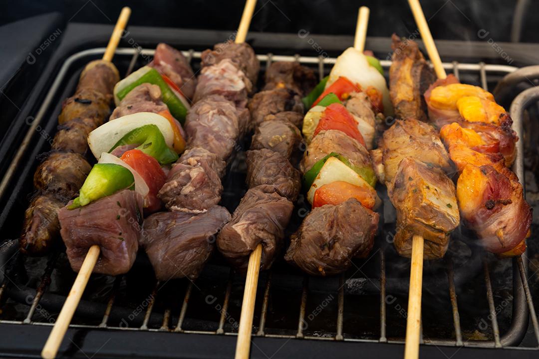 sete espetos em uma grelha elétrica, feitos de carne de porco, frango, cebola, pimenta, bovino