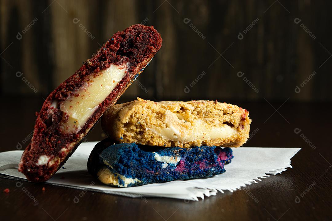 três biscoitos coloridos caseiros cortados ao meio em cima de uma superfície de madeira