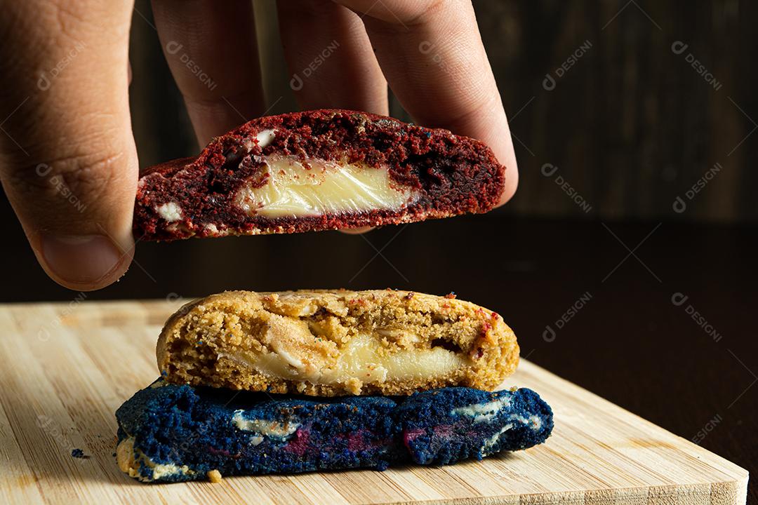 mão masculina pegando três biscoitos caseiros coloridos cortados ao meio em cima da superfície de madeira