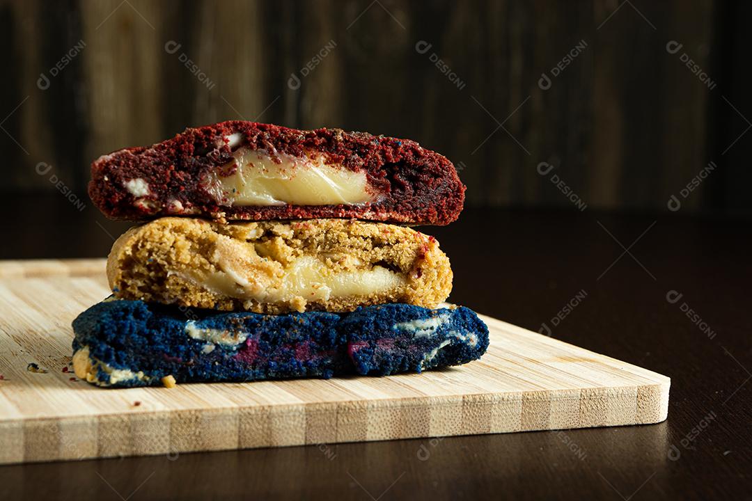 três biscoitos coloridos caseiros cortados ao meio em cima de uma superfície de madeira