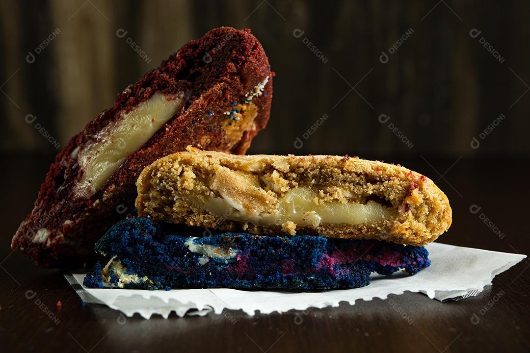 três biscoitos coloridos caseiros cortados ao meio em cima de uma superfície de madeira