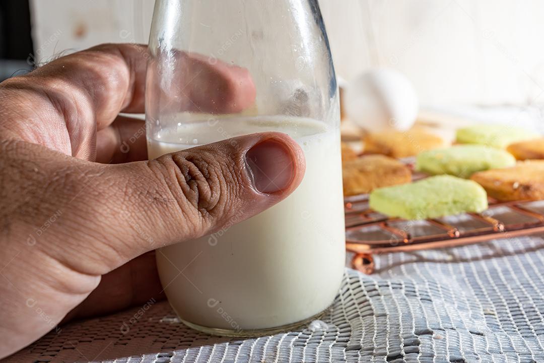 Mão masculina segurando fresco com leite em mesa de madeira com pano branco