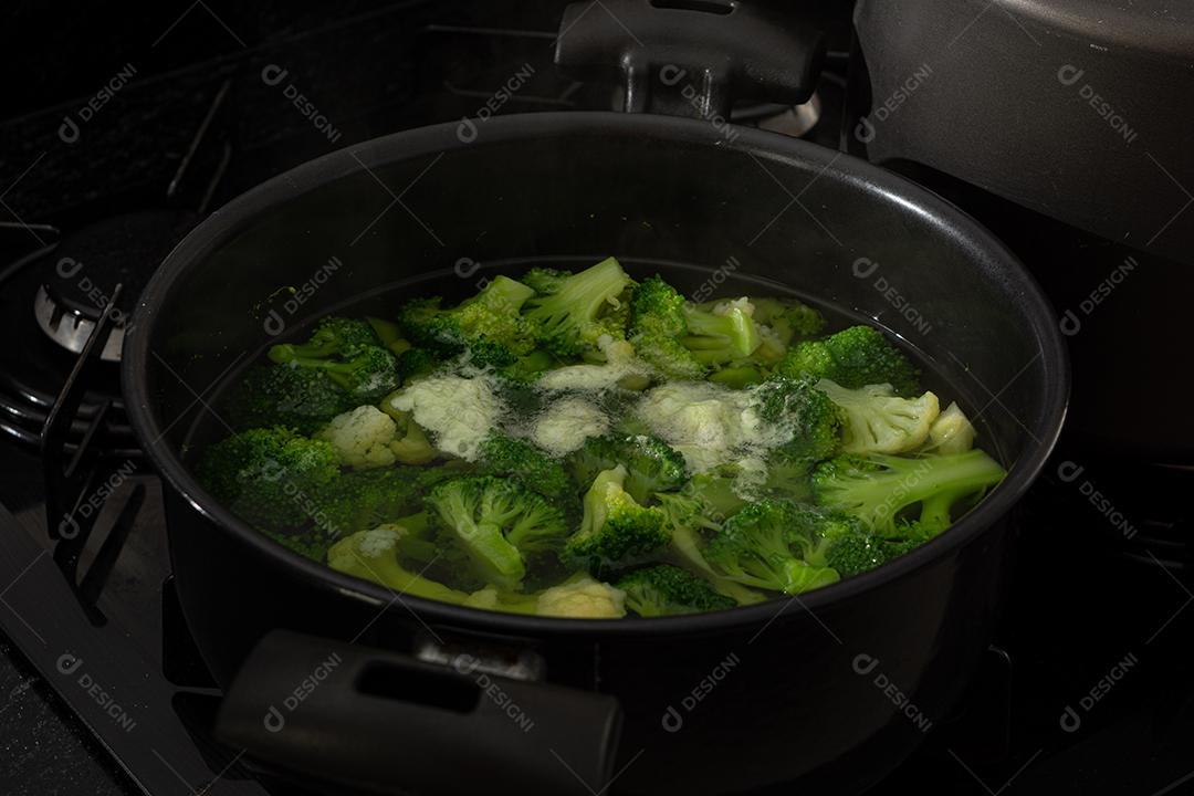 Brócolis com água em panela preto sobre fogão. Verdura