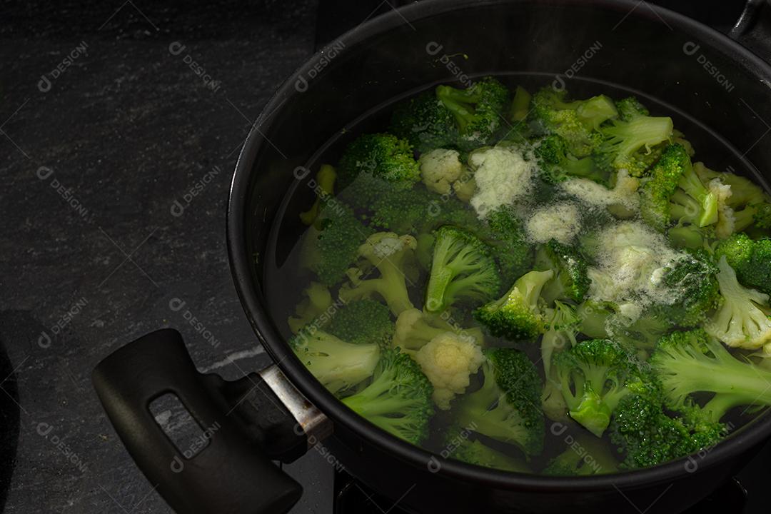 Brócolis com água em panela preto sobre fogão. Verdura
