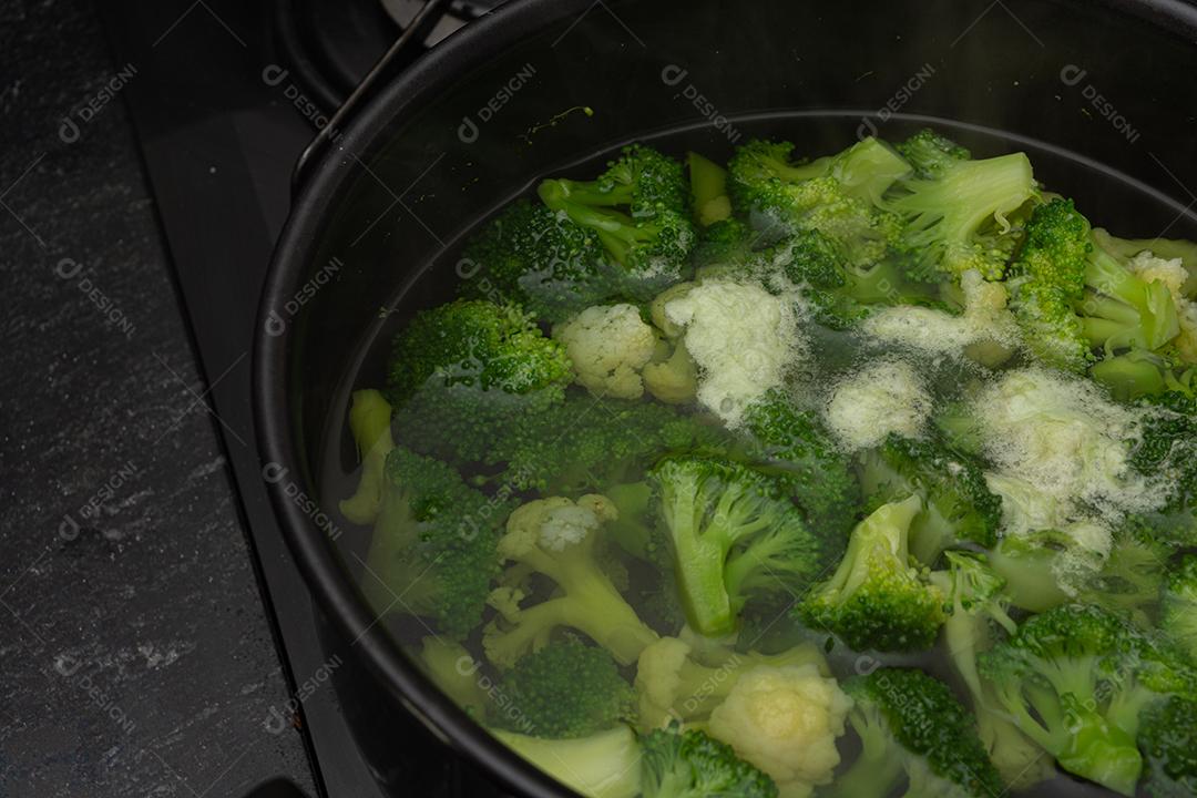 Brócolis com água em panela preto sobre fogão. Verdura