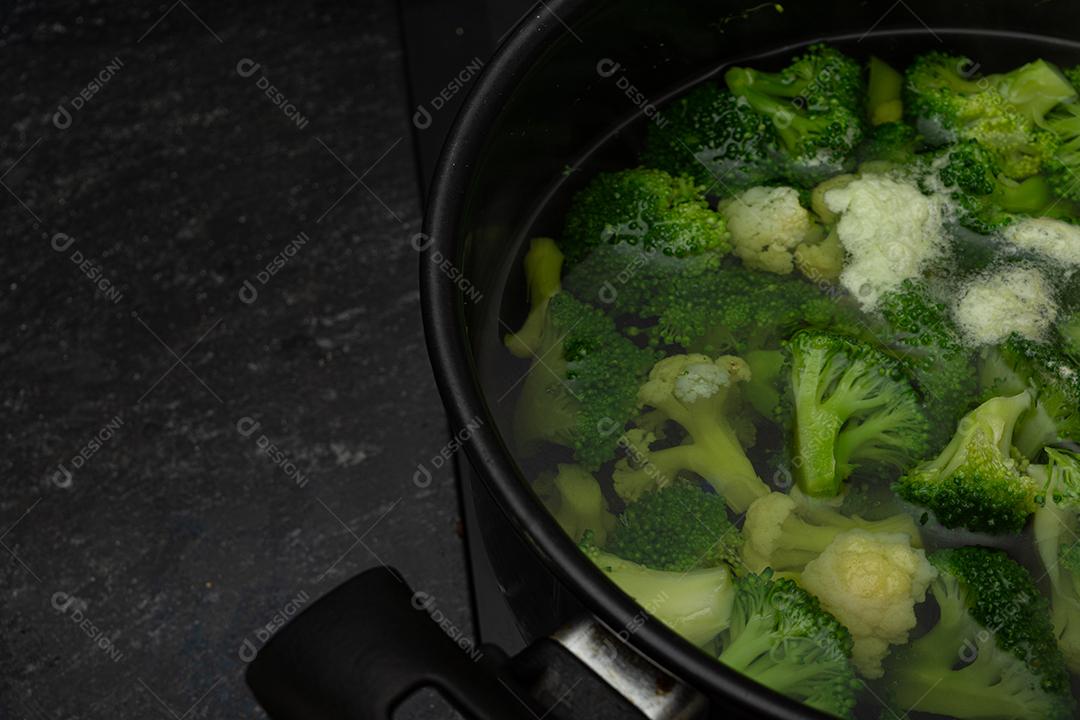 Brócolis com água em panela preto sobre fogão. Verdura