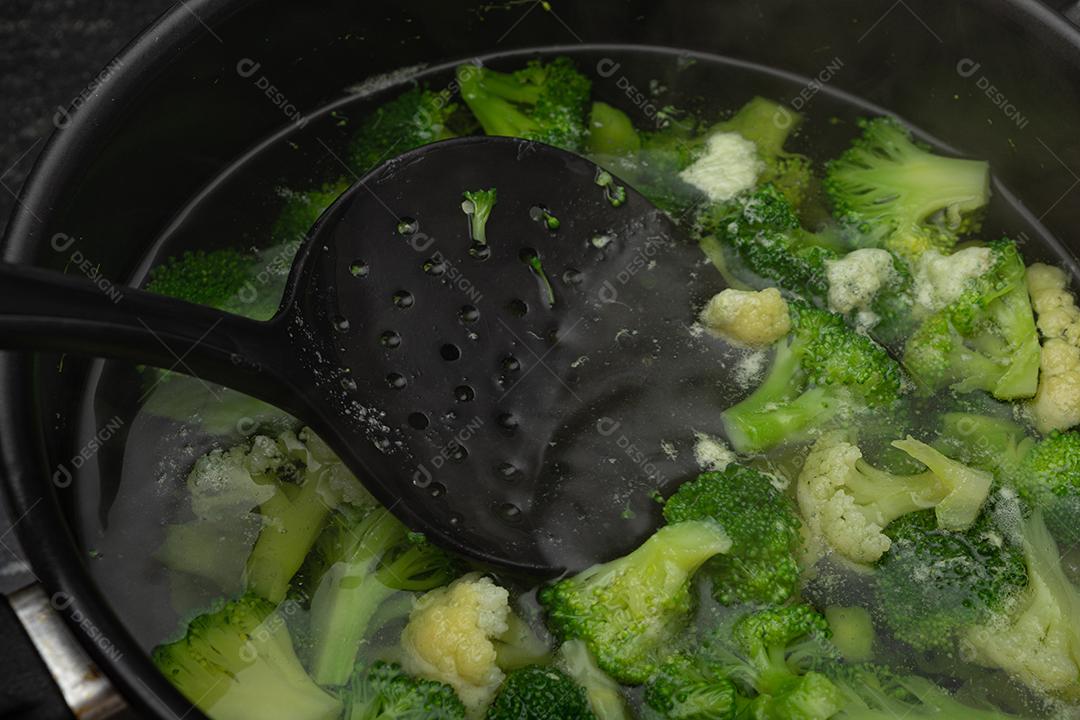 Brócolis com água em panela preto sobre fogão. Verdura