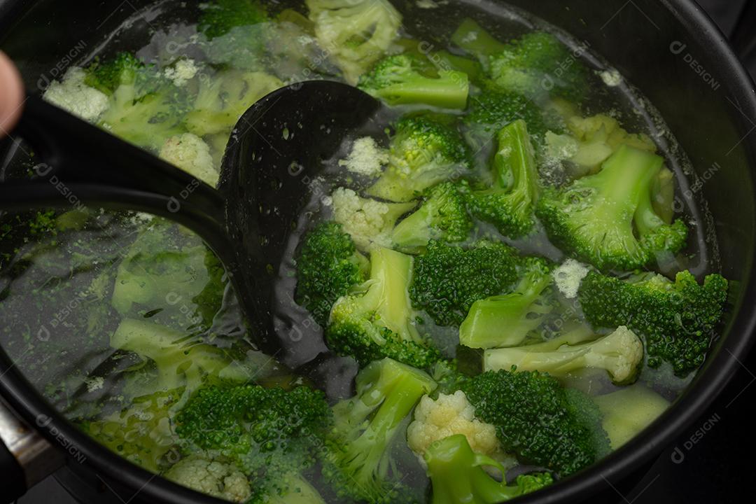 Brócolis com água em panela preto sobre fogão. Verdura