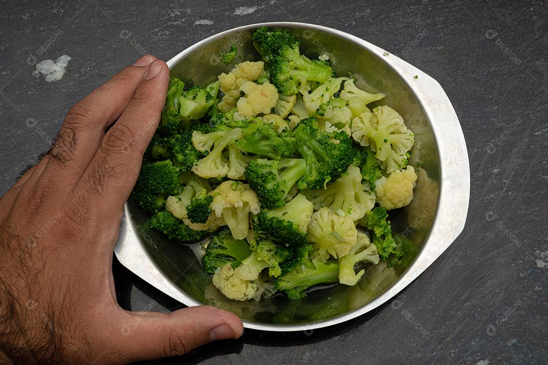 Mão segurando panela com brócolis cozidos. Verdura