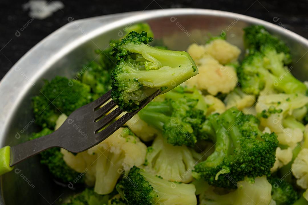 Brócolis cozidos com garfo sobre panela. Verdura