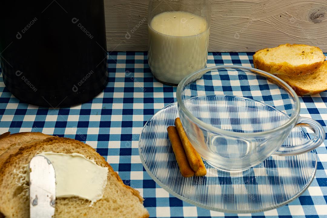 Pão com manteiga, leite, café em xícara, café da manhã, lanche sobre pano xadrez azul  mesa madeira