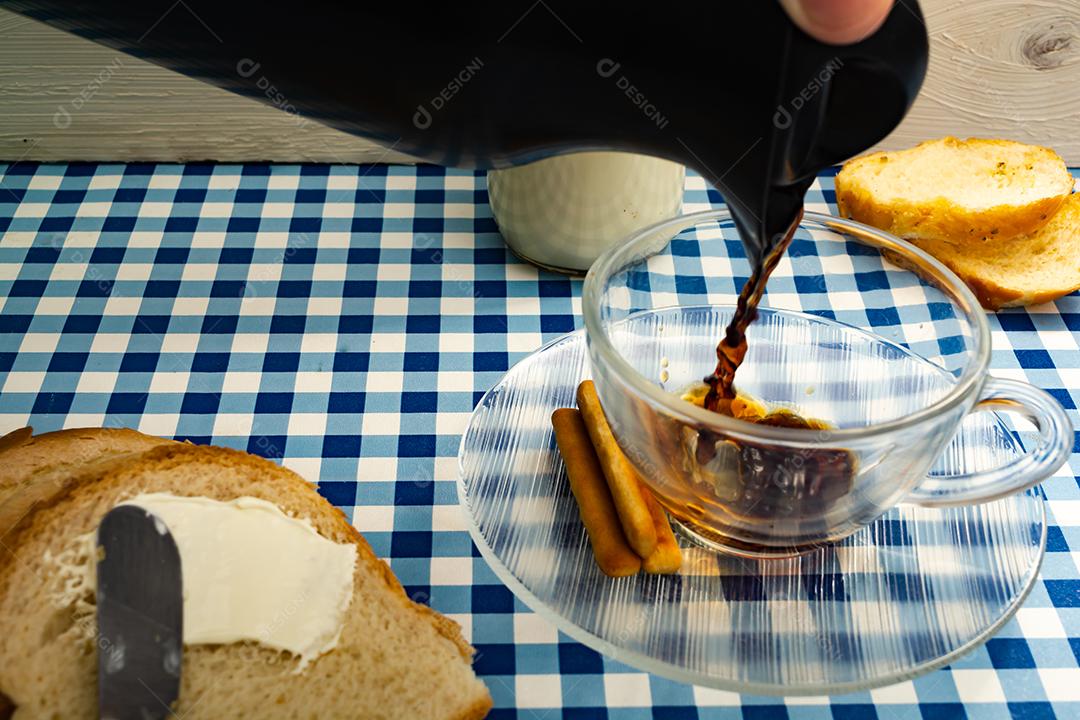 Pão com manteiga, leite, café em xícara, café da manhã, lanche sobre pano xadrez azul  mesa madeira