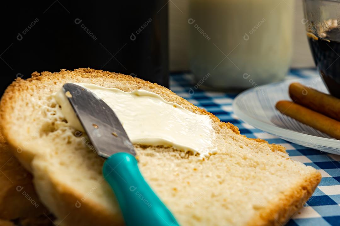 Pão com manteiga, leite, café em xícara, café da manhã, lanche sobre pano xadrez azul  mesa madeira