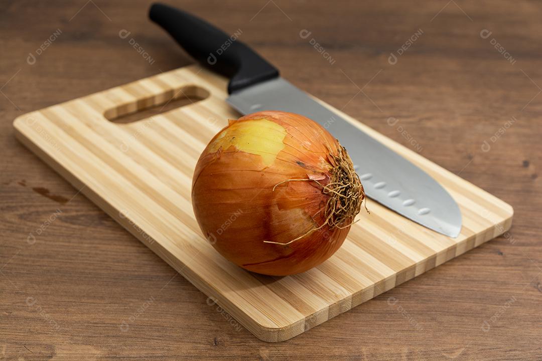 Cebola com faca sobre tabua e mesa de madeira, tempero.