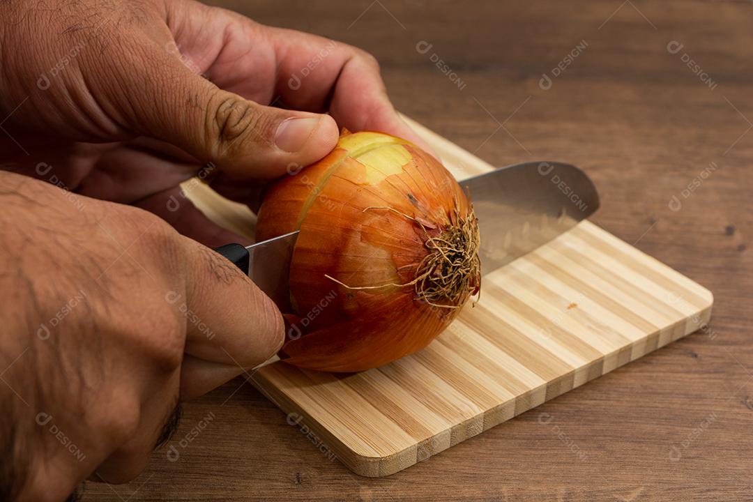 Mão segurando cebola sobre tabua e mesa de madeira, tempero.