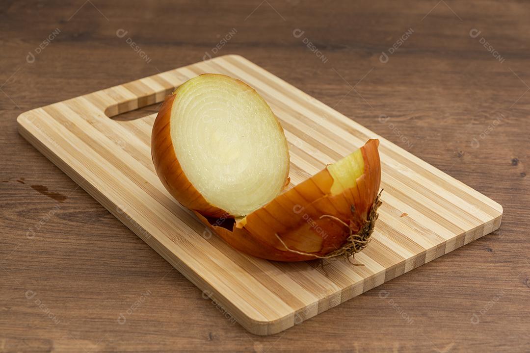 Meia cebola sobre tabua e mesa de madeira, tempero.