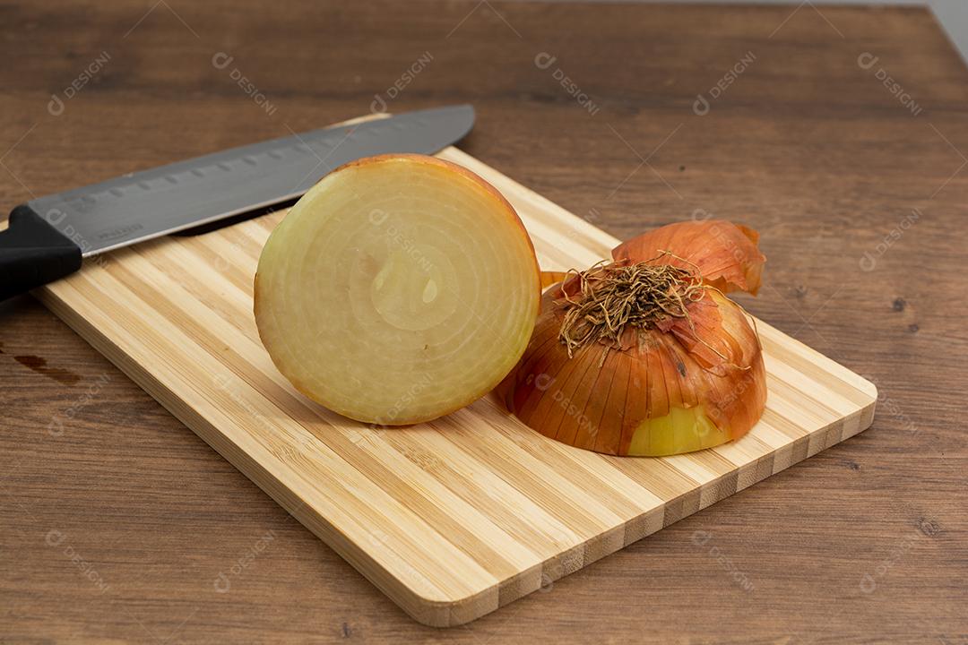 Meia cebola sobre tabua e mesa de madeira, tempero.