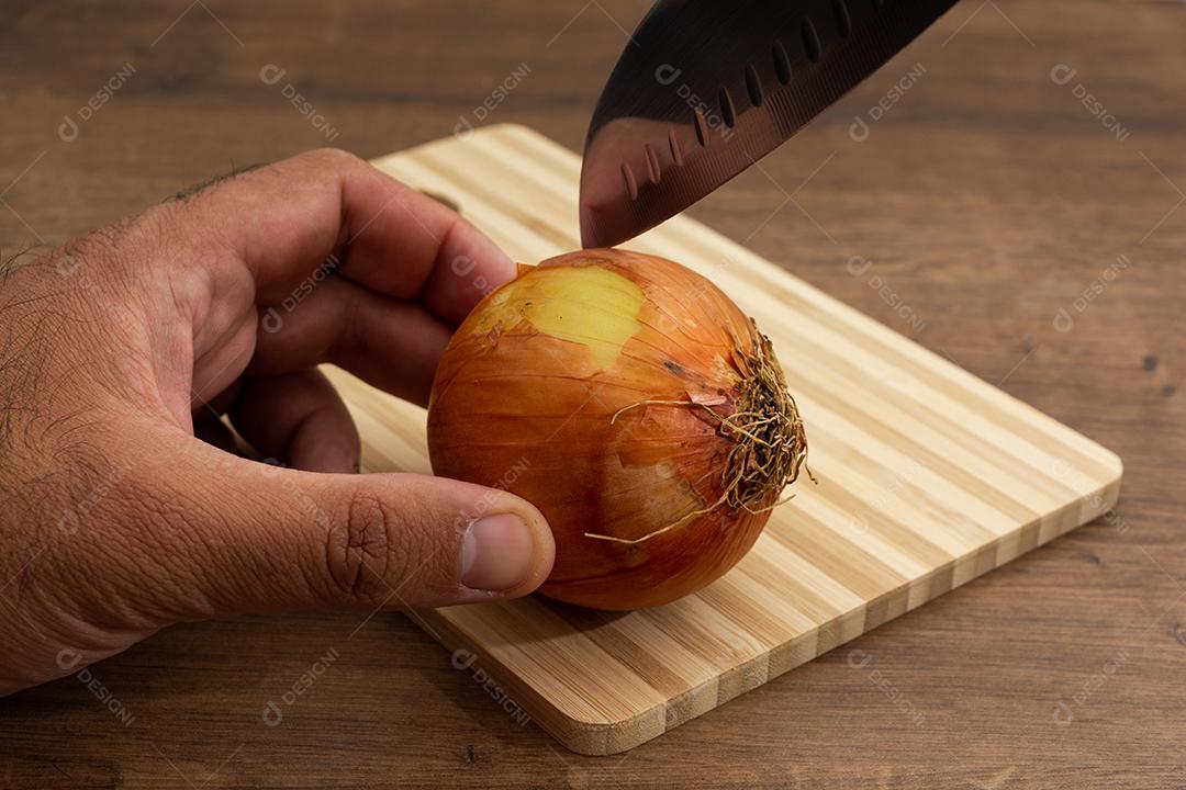 Cebola com faca sobre tabua e mesa de madeira, tempero.