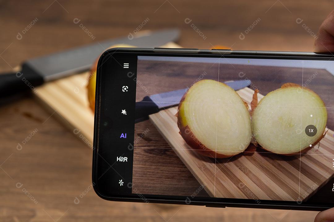 Meia cebola  no smartphone sobre tabua e mesa de madeira, tempero.