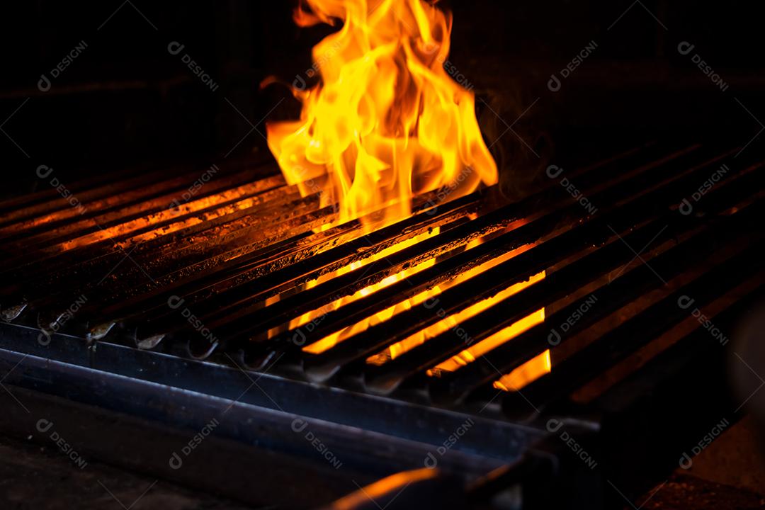 Fogo passando por grelha de churrasqueira sobre fundo preto.