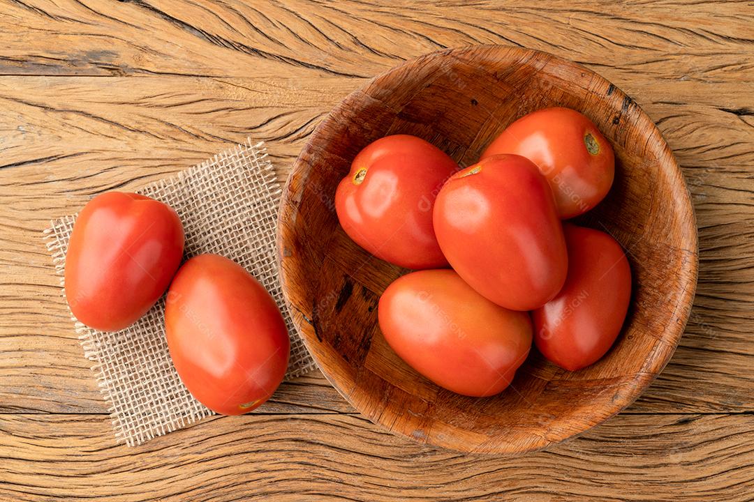 Tomates vermelhos em uma tigela sobre a mesa de madeira.