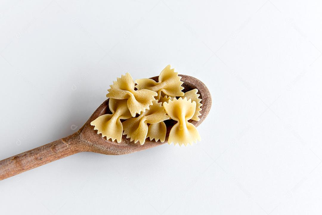 macarrão gravata cru na colher de pau e fundo branco (farfalle ita