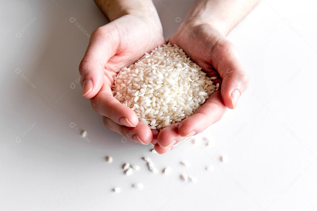 mãos segurando arroz arbóreo, arroz de risoto em fundo branco.