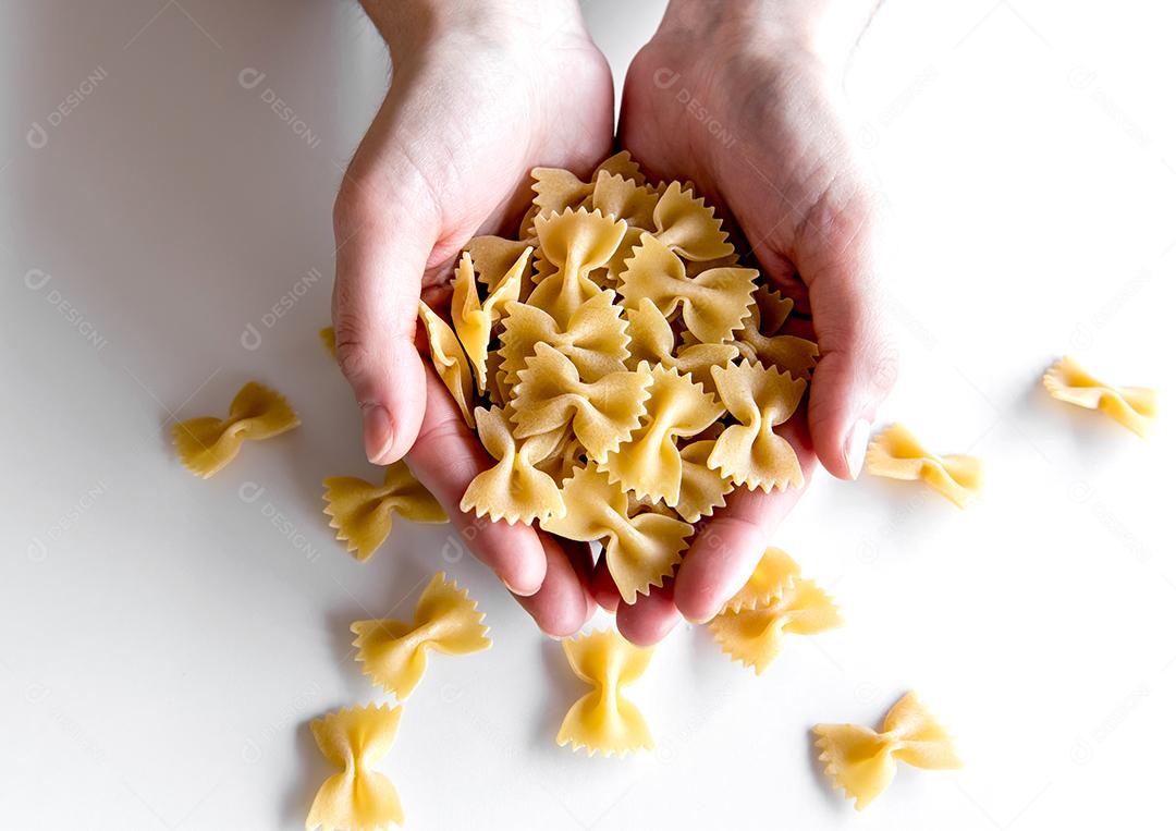 Mãos segurando macarrão italiano farfalle de gravata crua