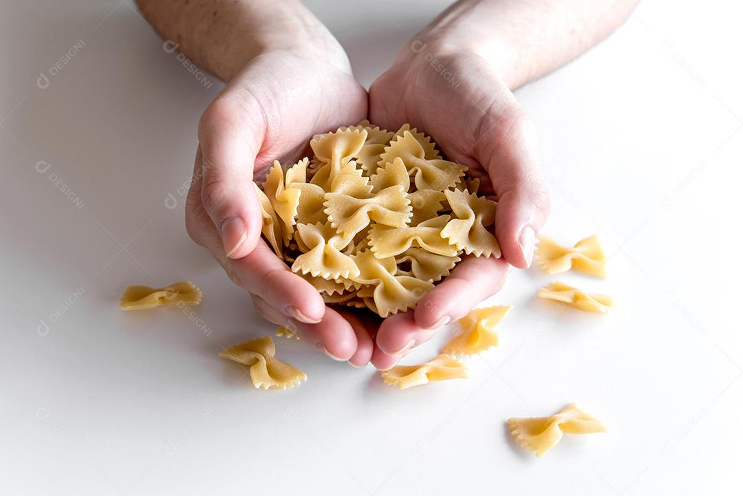 Mãos segurando macarrão farfalle de gravata crua