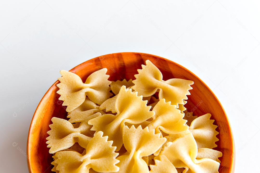 macarrão gravata cru em panela de madeira e fundo branco (massa farfalle)