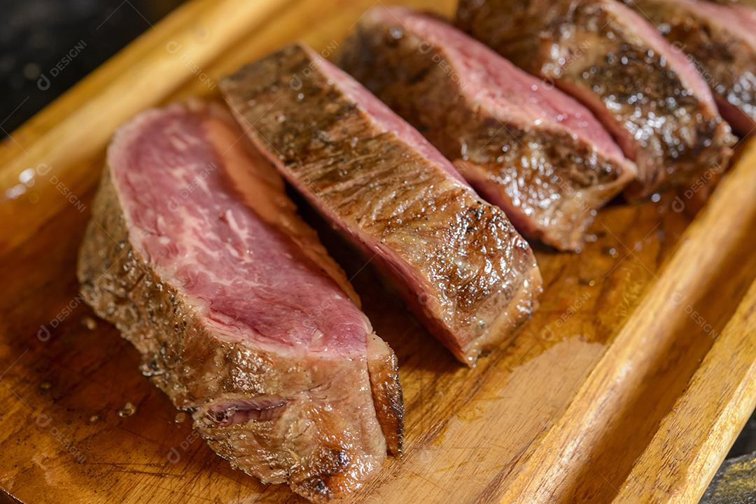 Churrasco de carne assada e fatiada na placa de madeira com fundo desfocado.