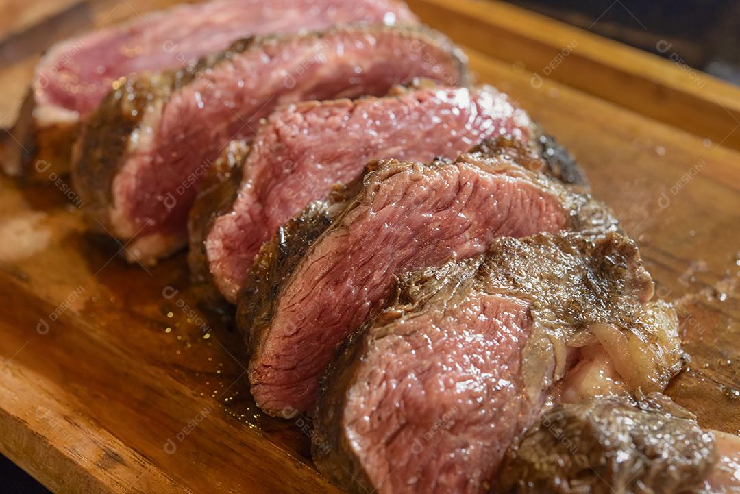 Churrasco de carne assada e fatiada na placa de madeira com fundo desfocado.