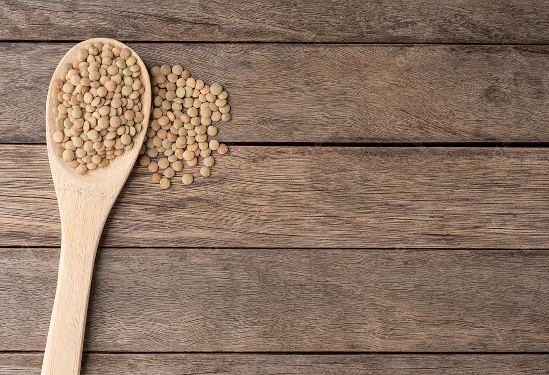 Lentilhas cruas em uma colher sobre a mesa de madeira