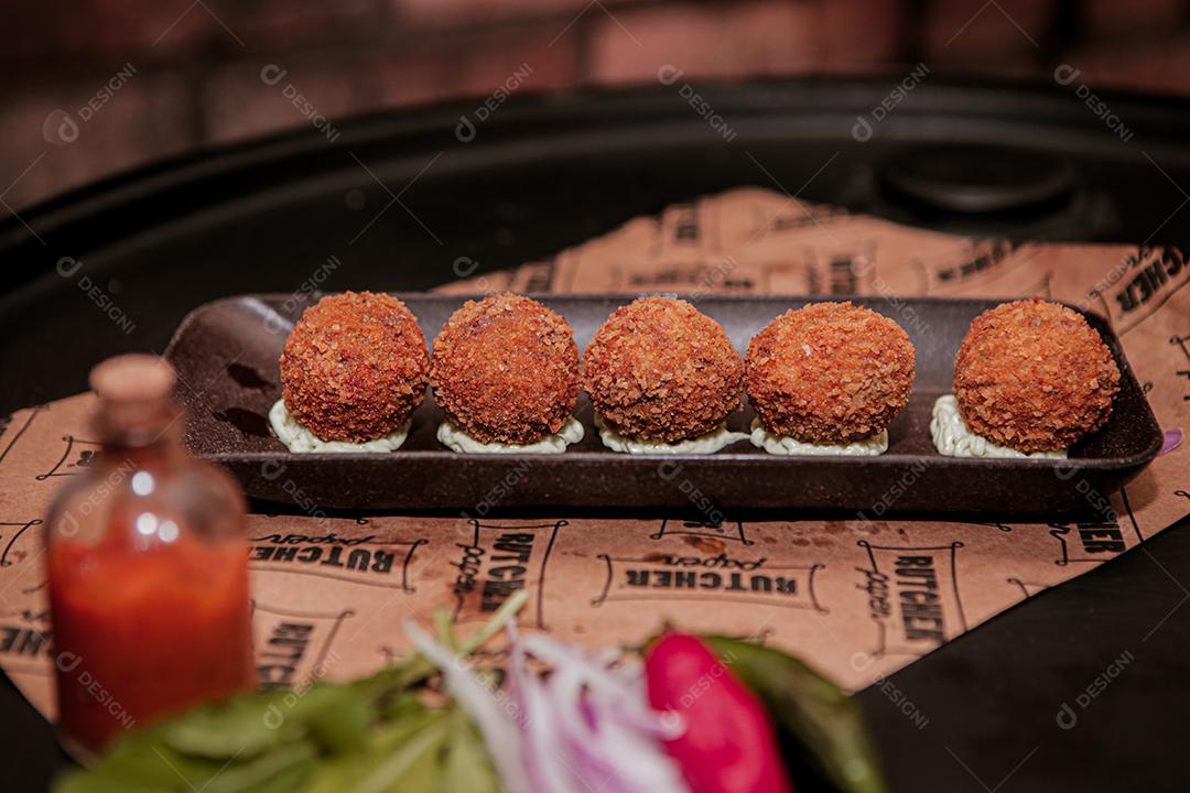 Salgados de carne com molho branco sobre fundo preto.