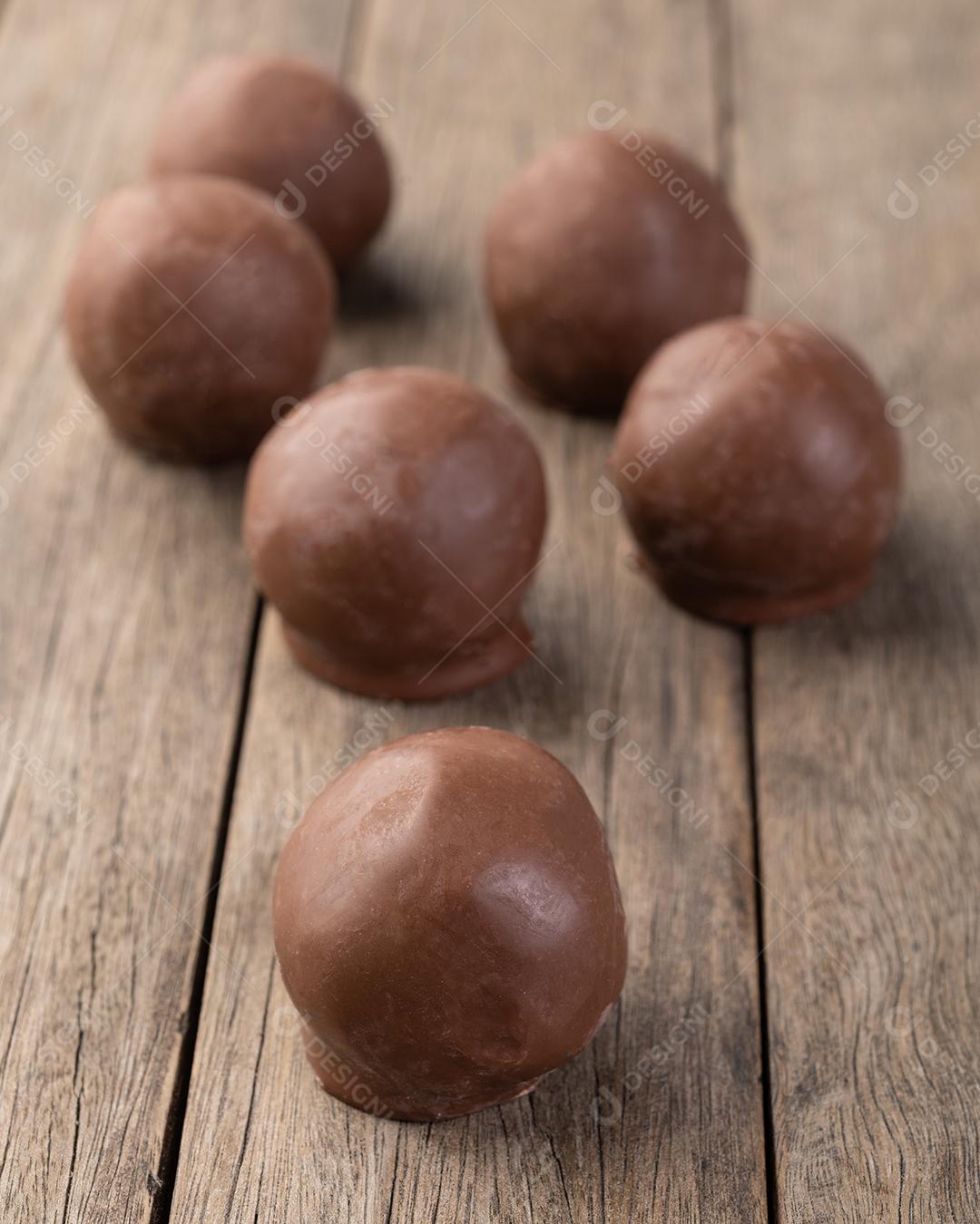 Doces de chocolate recheados com doces sobre placa de madeira.