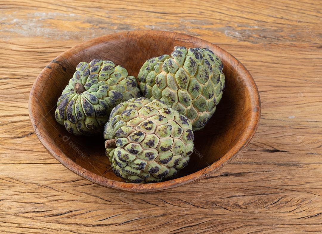 Maçãs de açúcar ou pinha em uma tigela sobre a mesa de madeira.