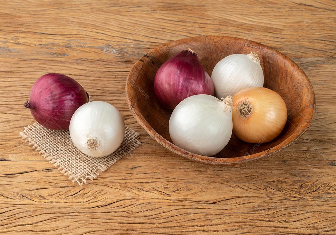 Cebolas variadas em uma tigela sobre a mesa de madeira.