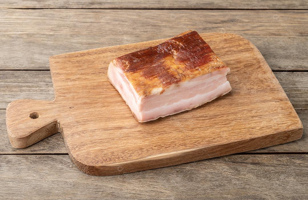 Pedaço de bacon defumado sobre tábua de madeira.
