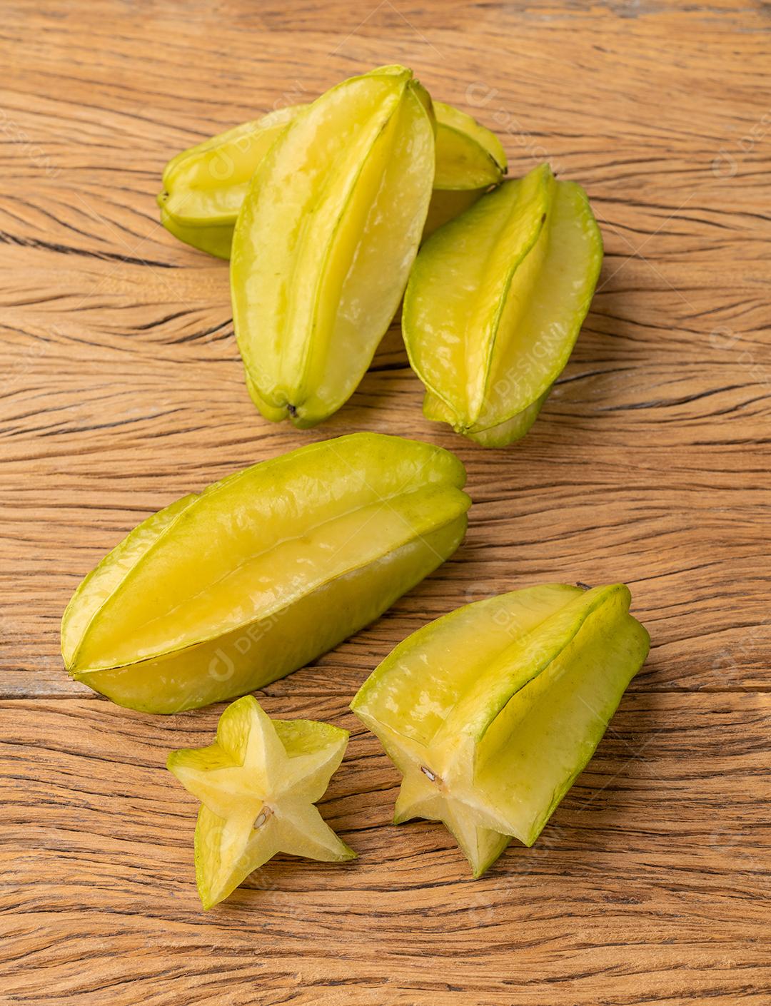 Um grupo de frutos de estrela com fatias sobre a mesa de madeira.