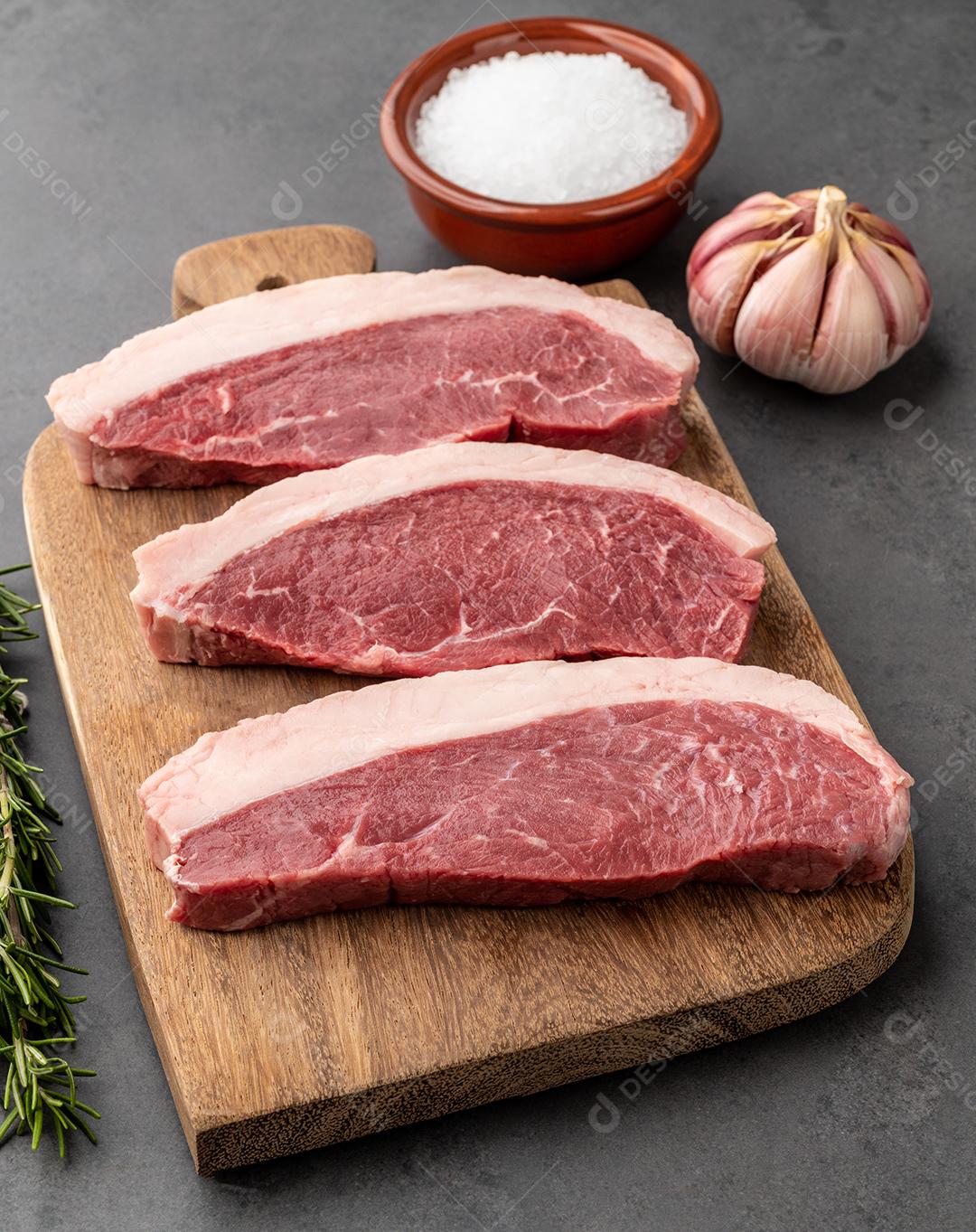 Picanha crua fatiada ou carne de alcatra sobre tábua de madeira com temperos.